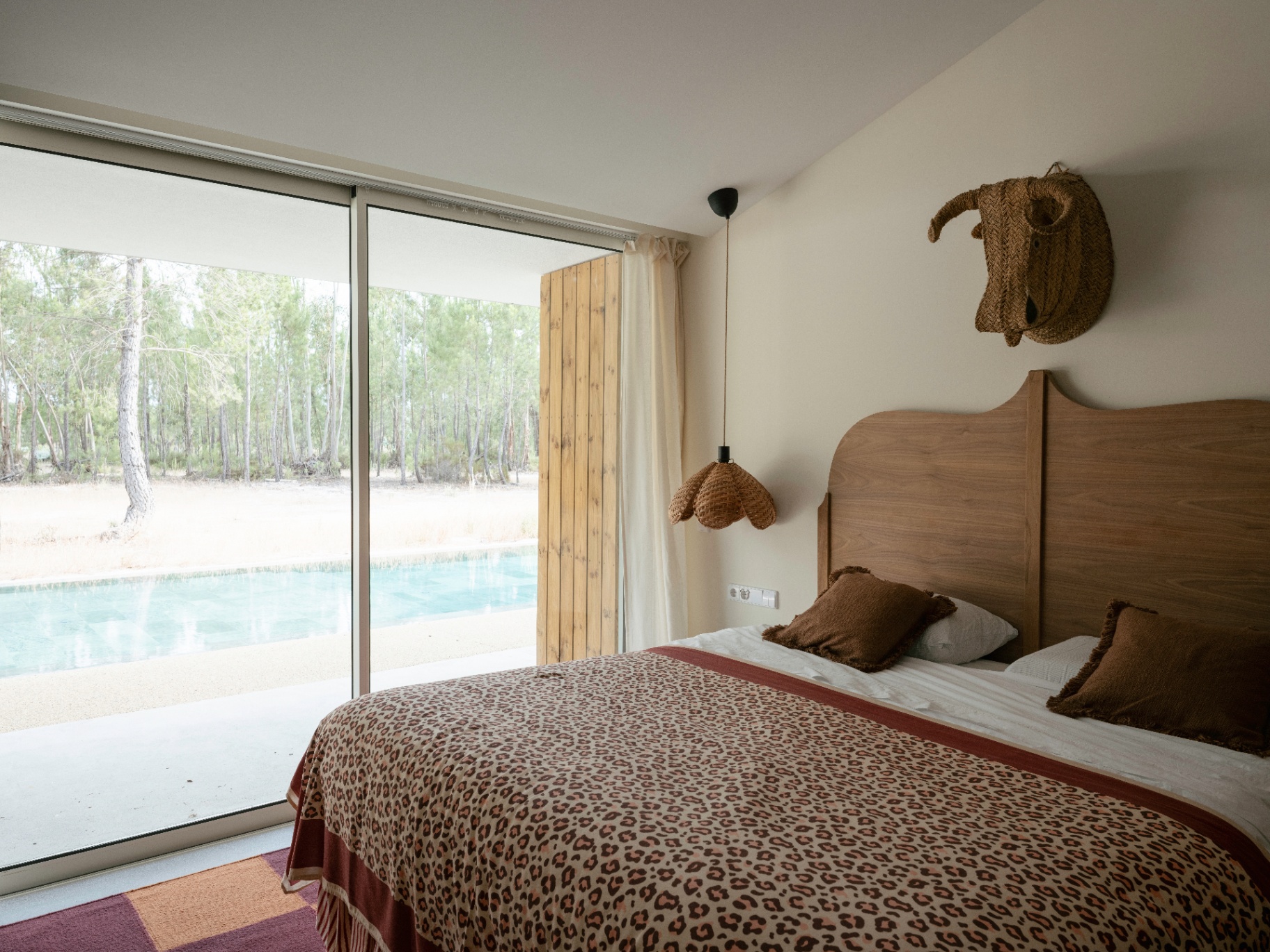 Bedroom with leopard-print throw and full-height window onto the pool and pinewood.