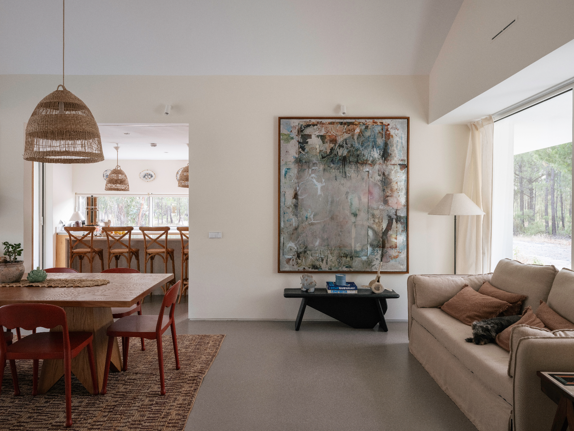 Open living and dining room with a large abstract painting and rattan pendants.