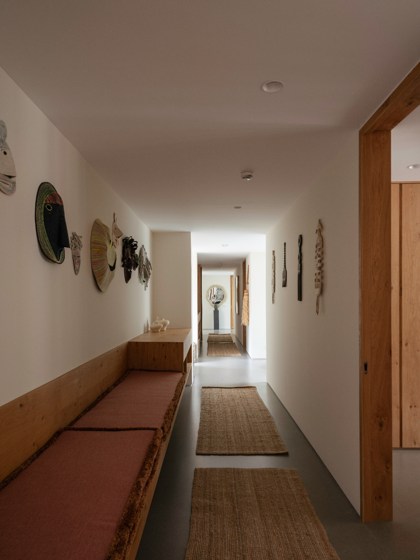 Hallway hung with a collection of carved masks above a long banquette.